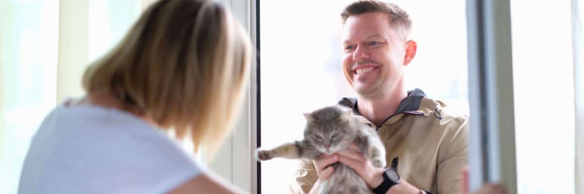 Man giving grey cat to woman through door